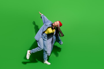 Full size photo of attractive young woman dance have fun chilling wear trendy jeans clothes isolated on green color background