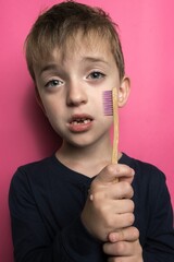 a boy of Slavic appearance holds a bamboo toothbrush in his hands. baby teeth