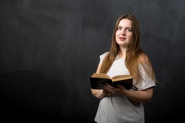 a woman of European appearance holds a book in her hands against the background of a black slate wall.