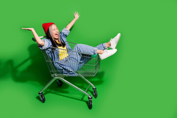 Full body photo of attractive young woman shopping cart have fun excited wear trendy jeans clothes isolated on green color background