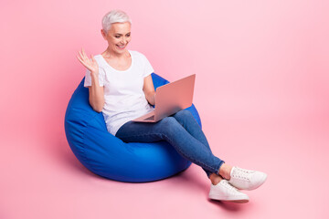Full size photo of attractive charming woman wear white t-shirt sit on bean bag say hi on laptop...