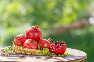 Pomegranate in wooden basket on wooden table in garden, Pomegranate with slices on blurred greenery background.