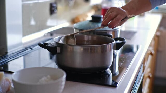 Caucasian Woman Stirring Tomato Soup Cooked in Metal Pot on Kitchen Stove Cooker