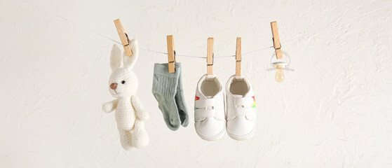 Stylish baby shoes with socks and cute toy hanging on rope against white grunge background