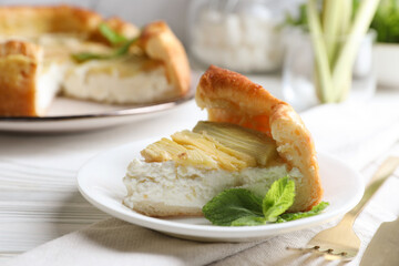 Piece of freshly baked rhubarb pie with cream cheese, mint leaves and cutlery on white wooden table, closeup