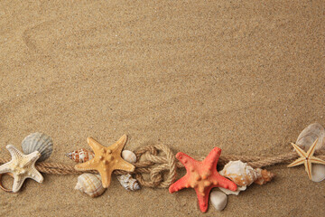Fototapeta na wymiar Beautiful sea stars, shells and ropes on sand, flat lay. Space for text