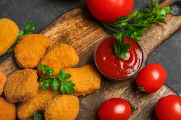 Wooden board with tasty nuggets and ketchup on dark background