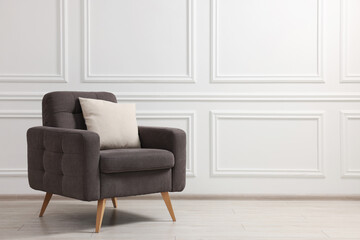 Stylish armchair with cushion near white wall indoors, space for text