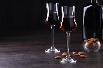 Liqueur glasses with tasty amaretto and almonds on wooden table, space for text