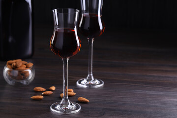 Liqueur glasses with tasty amaretto and almonds on wooden table, space for text