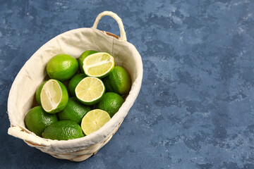 Basket with fresh limes on blue background