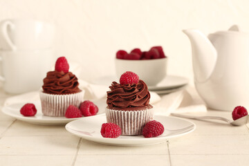 Plates of tasty chocolate cupcakes with raspberries on table