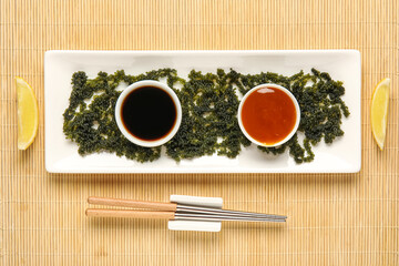 Composition with plate of healthy seaweed, sauces and chopsticks on bamboo mat