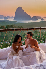 A couple in an outdoor bedroom watching the sunrise over Sametnangshe mountains in Phangnga Bay...