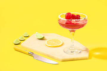 Glass of Cosmopolitan cocktail with cherries and lemon on yellow background