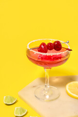 Glass of Cosmopolitan cocktail with cherries and lime on yellow background