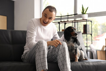 Young man with cute cocker spaniel sitting on couch at home