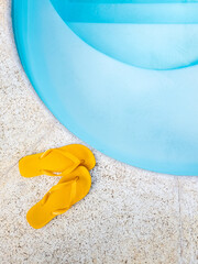 um par de chinelos amarelos perto da borda da piscina, a piscina é de azul claro e tem água...