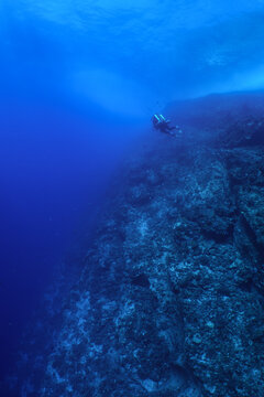 Scuba diver swim along a tropical wall near Maui, wearing a closed circuit rebreather. A rocky reef grows on the back wall at molokini crater.