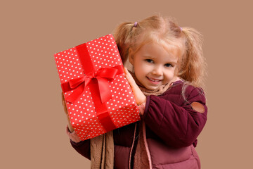 Cute little girl in winter clothes with gift box on beige background