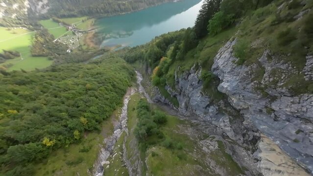 FPV drone descend over Switzerland mountain gorge and reach turquoise water lake