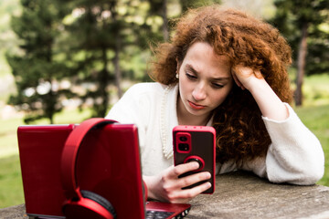 Redhead woman studying outdoors with her computer and mobile phone