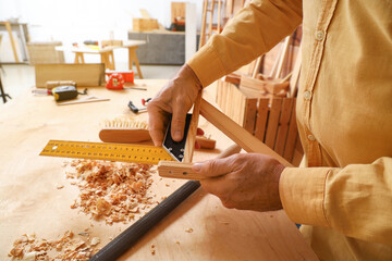 Mature carpenter measuring wooden plank in shop, closeup