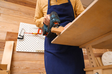 Mature carpenter sawing wooden plank with jigsaw at table in workshop, closeup