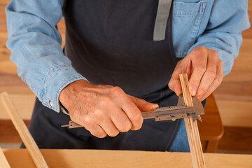 Mature carpenter measuring wooden plank at table in shop, closeup