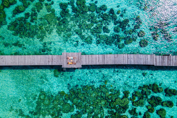 couple at a wooden pier in the ocean of Koh Kham Trat Thailand, aerial view of the tropical island near Koh Mak Thailand. top view at a man and woman lying down on a wooden jetty, bird eye view