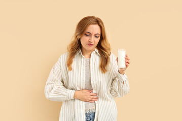 Mature woman with glass of milk suffering from stomachache on beige background