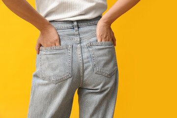 Beautiful young Asian woman in stylish jeans on yellow background, back view