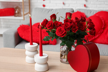 Bouquet of beautiful roses with gift box and candles on table in room decorated for Valentine's Day celebration