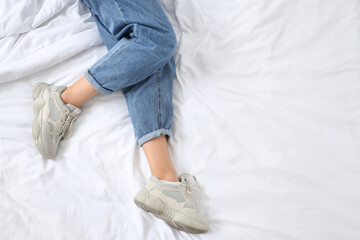 Young woman in trendy jeans lying on bed, top view