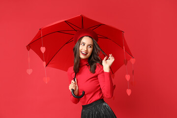 Beautiful young woman holding umbrella with paper hearts on red background. Valentine's Day celebration
