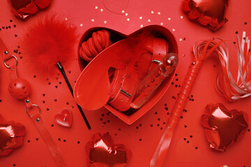 Gift box with different sex toys and heart shaped air balloons on red background. Valentine's Day celebration