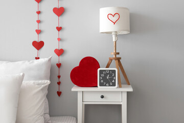 Bedside table with alarm clock, lamp and heart-shaped gift box in bedroom. Valentine's Day...