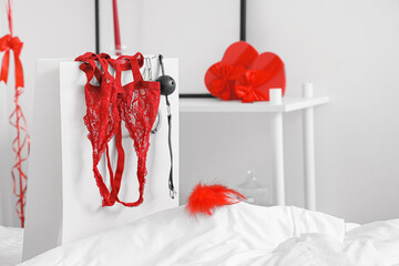 Shopping bag with red lingerie and sex toys on white bed, closeup. Valentine's Day celebration