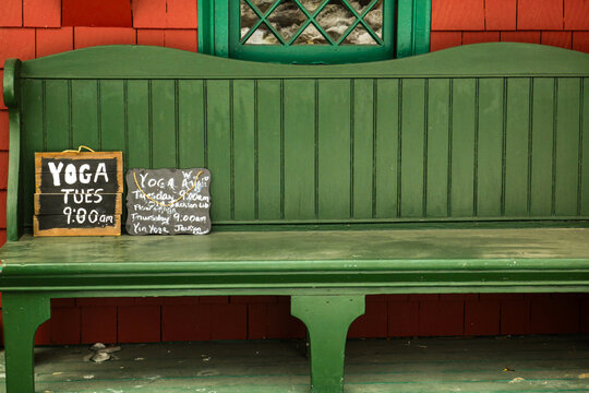 green wooden bench with yoga announcements on wooden and slate boards in front of green window and red shingle siding 
