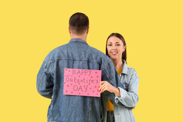 Lovely couple holding greeting card with text HAPPY VALENTINE'S DAY on yellow background