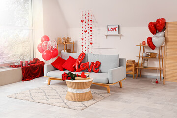 Interior of festive room with grey sofa, word LOVE made from balloons and bouquet of roses on coffee table. Valentine's Day celebration