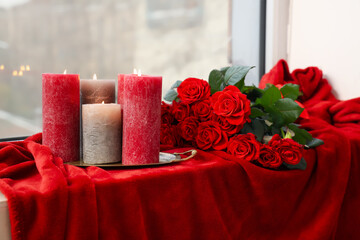 Red blanket with burning candles and bouquet of beautiful roses on windowsill. Valentine's Day...