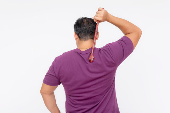 A middle aged man using a backscratcher to scracth and relieve an itch on his upper back. Rear view, isolated on a white background.
