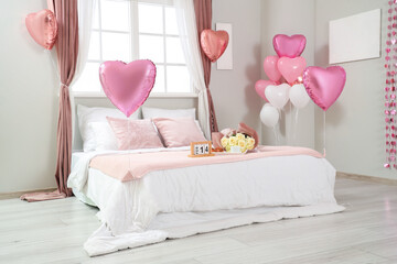 Interior of festive bedroom with heart-shaped balloons and bouquet of roses on bed. Valentine's Day...