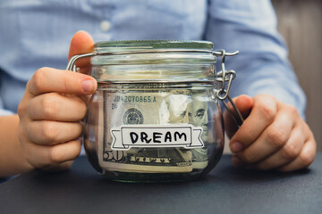 Female hands holding Glass jar full of American currency dollars cash banknote with text DREAM....