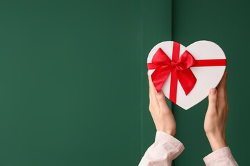 Female hands with gift box on green background. Valentine's Day celebration
