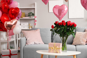 Vase with bouquet of beautiful roses and gift box on coffee table in living room. Valentine's Day celebration