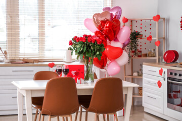 Dining table with bouquet of roses, wine glasses and gift boxes in light kitchen. Valentine's Day celebration