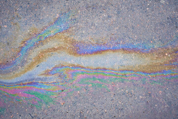 Multi-colored poisonous spots of spilled gasoline on wet pavement during rain.