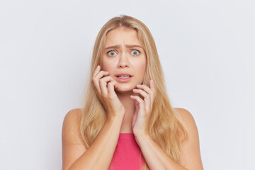 Young fair-haired woman with scared expression on face stands on white studio background, hard day concept, copy space